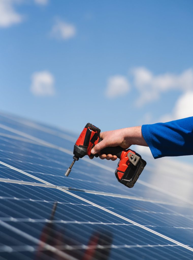 Close up view of engineer working with electric screwdriver drill installing solar panel to metal base