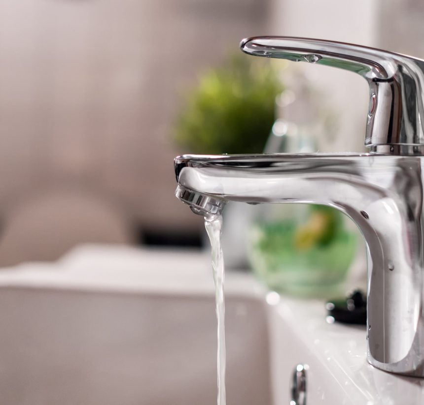 Cold water flowing from faucet in clean bright bathroom